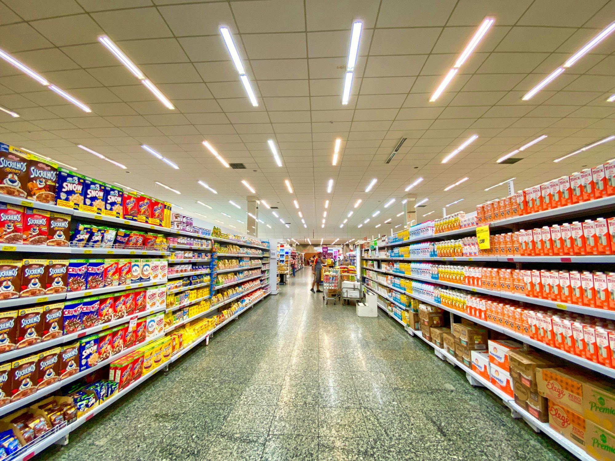 Image of an empty aisle in a grocery store. The shelves are neatly and fully stocked