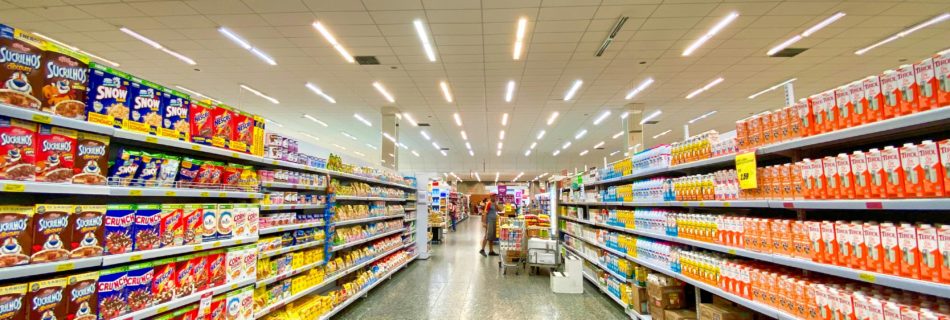 Image of an empty aisle in a grocery store. The shelves are neatly and fully stocked